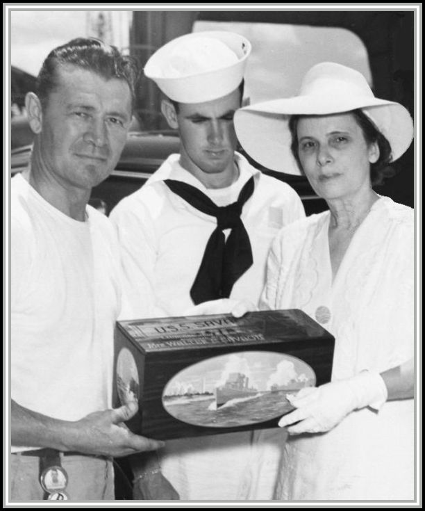 photograph of ship's foreman presenting Mrs. Savage with sea chest containing broken champagne bottle.  John Savage looks on in middle.